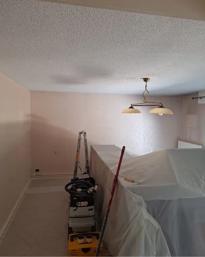 Séjour en cours de rénovation à Eysines. Murs enduits, mobilier protégé sous bâche, matériel de ponçage Mirka