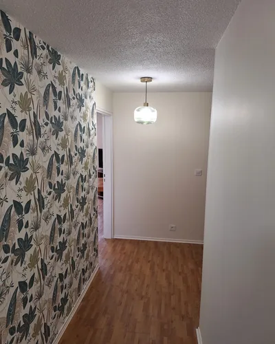 Couloir rénové à Eysines. Papier peint feuillage tropical à raccord, mur opposé velours blanc, parquet chêne